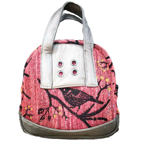 Un mini sac à main fabriqué à partir de chutes d'écharpe de portage montrant des oiseaux dans un arbre dans des tons roses et noirs, et du cuir d'agneau gris.