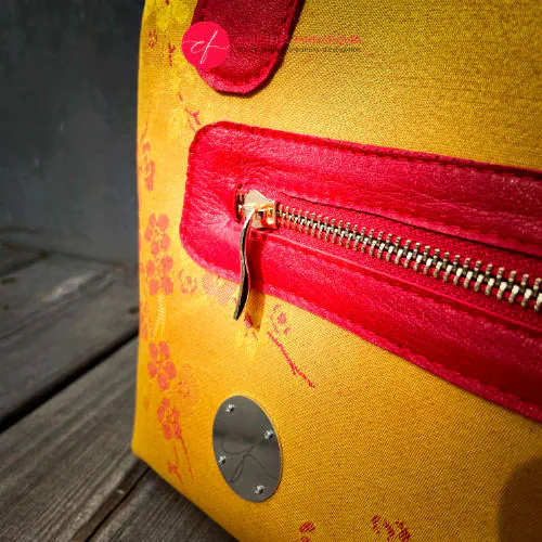 Un mini sac à main constitué de tissu d'ameublement jaune motif fleurs de cerisier rouge et de cuir rouge.