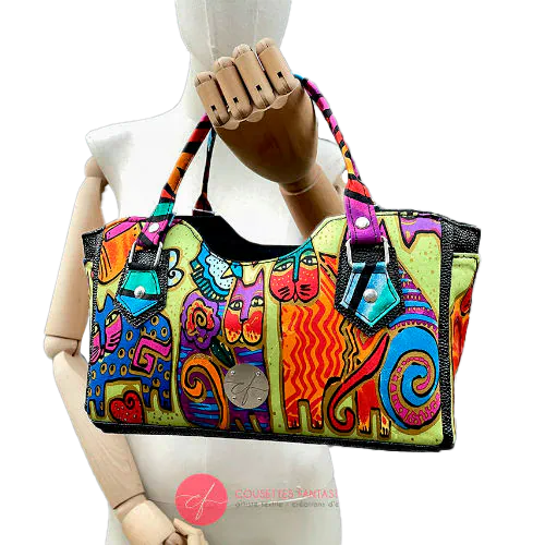 Un petit sac à main constitué d'un simili noir brillant texture galuchat et d'un foulard de soie au motif de chats très colorés.