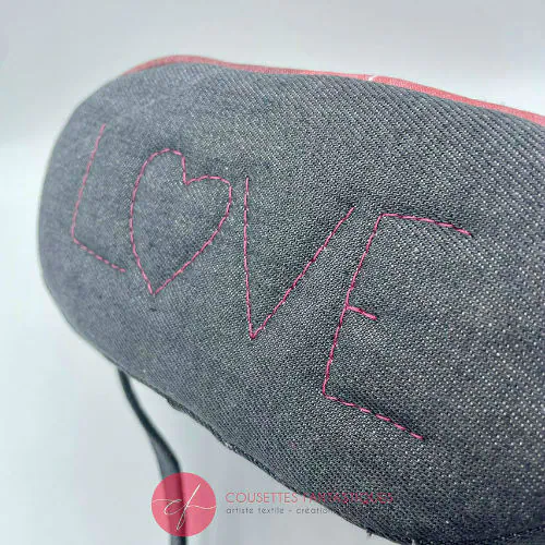 Un petit sac dit “seau” fait avec toile fine rose présentant deux silhouettes de cerfs blanches, et du denim haute-couture gris.