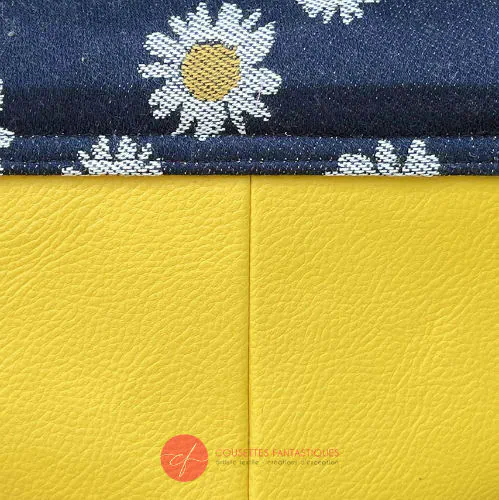 Un petit sac en simili jaune et un coupon de tissu d'écharpe avec des marguerites blanches et jaunes sur un fond bleu marine.