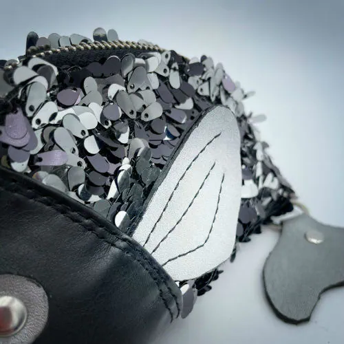 Une pochette zippée cousue dans du simili cuir noir, du tissu à sequins noirs et blancs, et du denim gris.