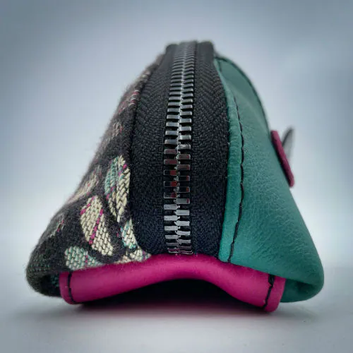 Une pochette zippée cousue dans un cuir vert sauge, un cuir vernis noir, un cuir rose fuschia et deux chutes d'écharpe de portage au motif de mailles vertes, beiges et roses sur fond noir.